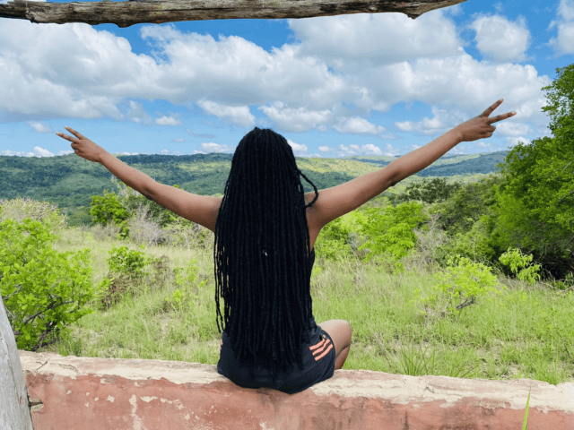 A-young-woman-with-long-black-hair-_dreadlocks_-and-arms-stretches-sitting-on-a-concrete-wall-overlooking Shimba Hills