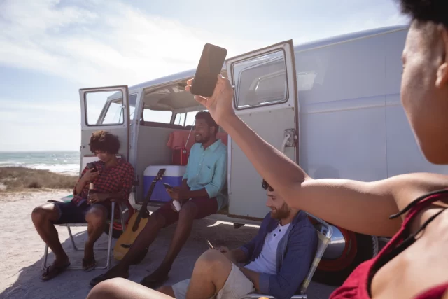 young man looking for wifi while his friends are sitting outside a camping van