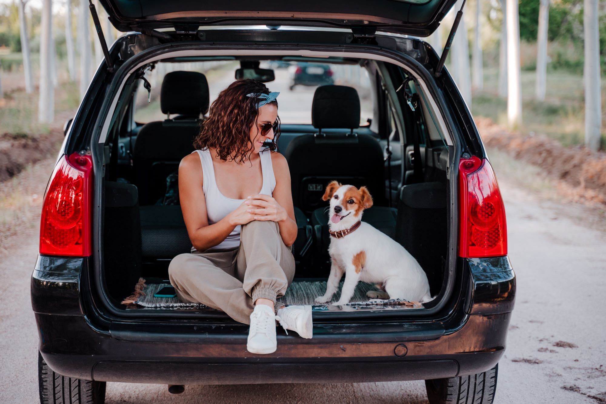 happy-woman-and-dog-relaxing-on-car-trunk-at-forest