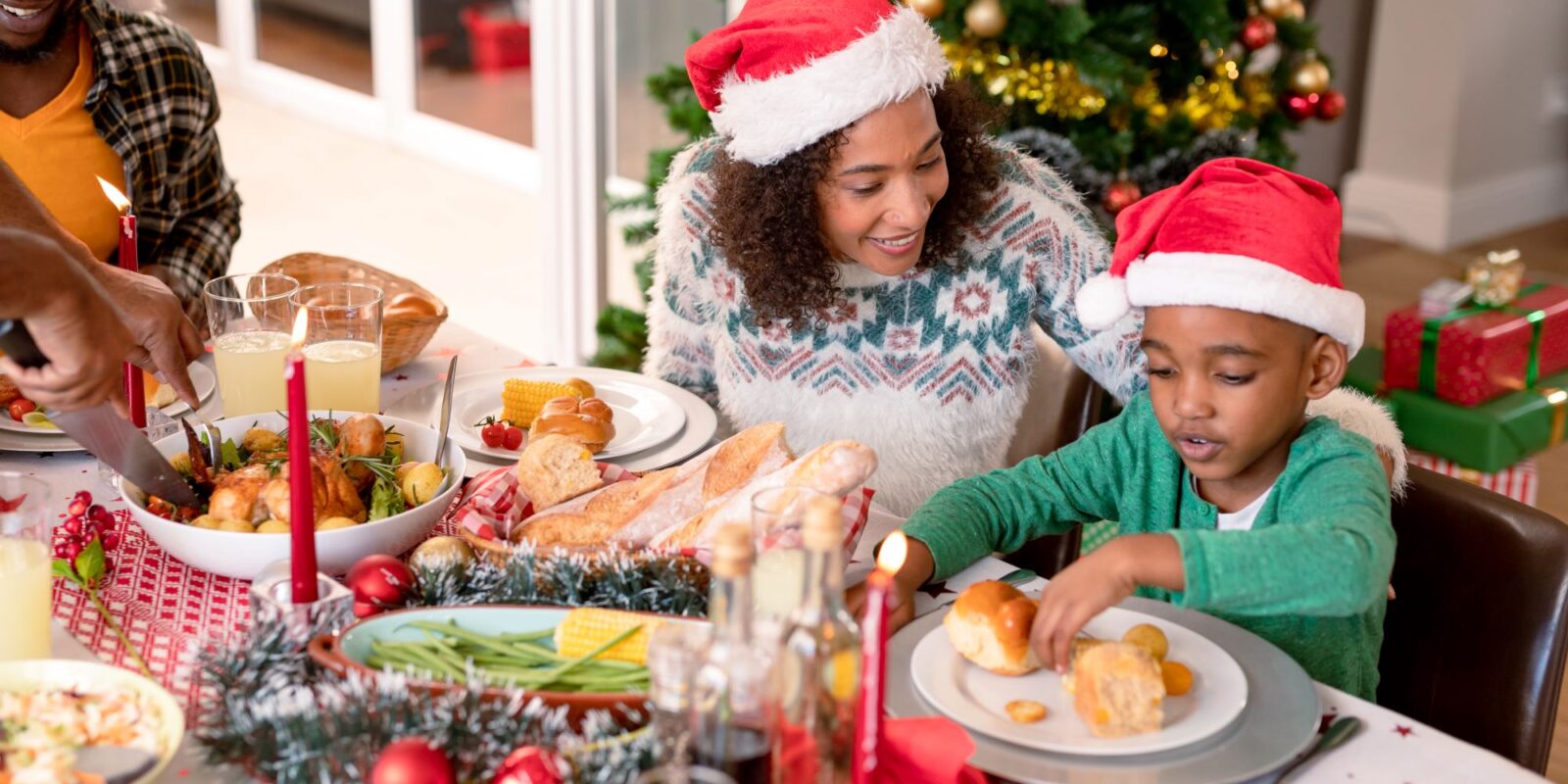 Happy african american mother and son wearing santa hats at christmas table-Authentic Breakfast Meals