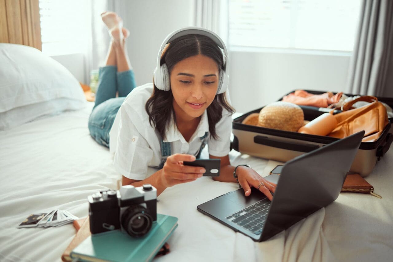 Travel, woman and bedroom booking on laptop with credit card for holiday planning with music stream