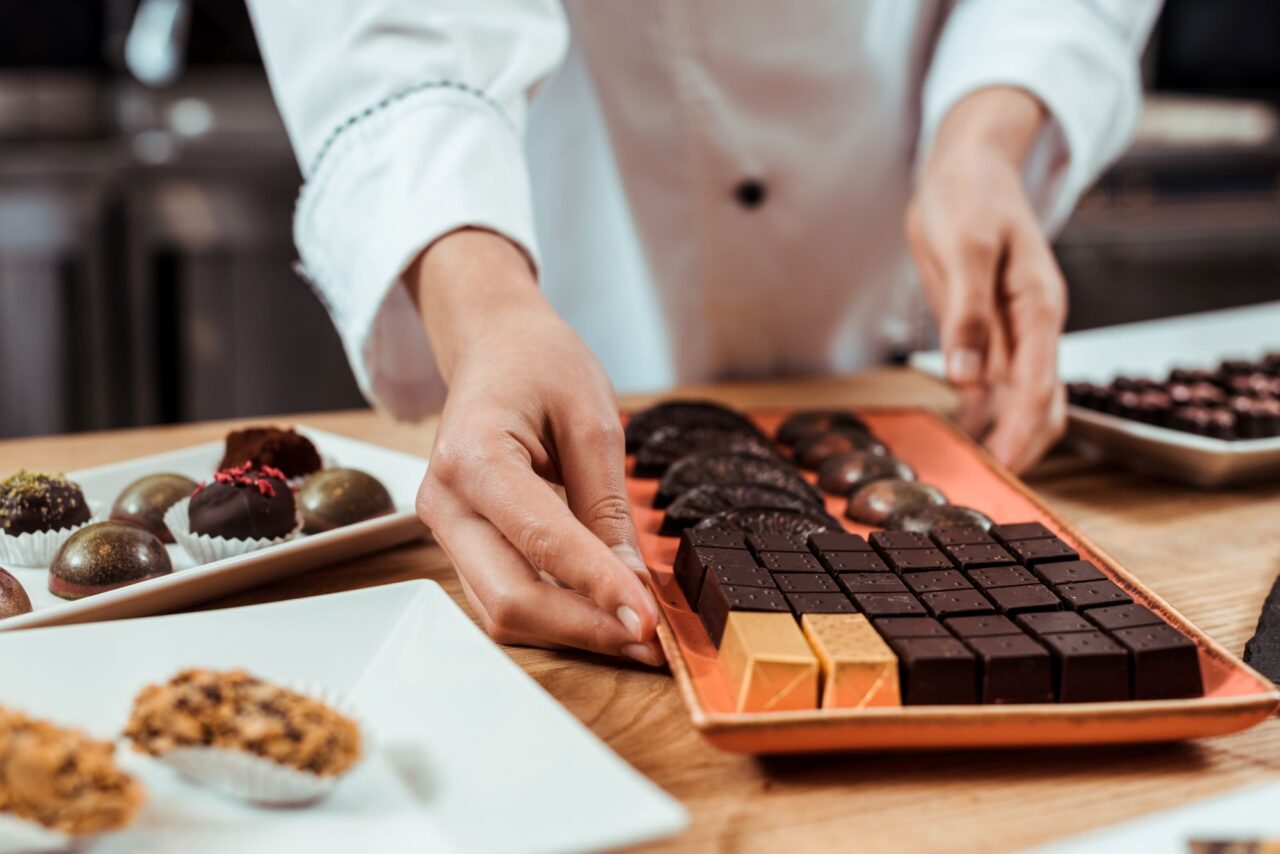 cropped view of chocolatier touching plate with tasty chocolate candies near chocolate balls