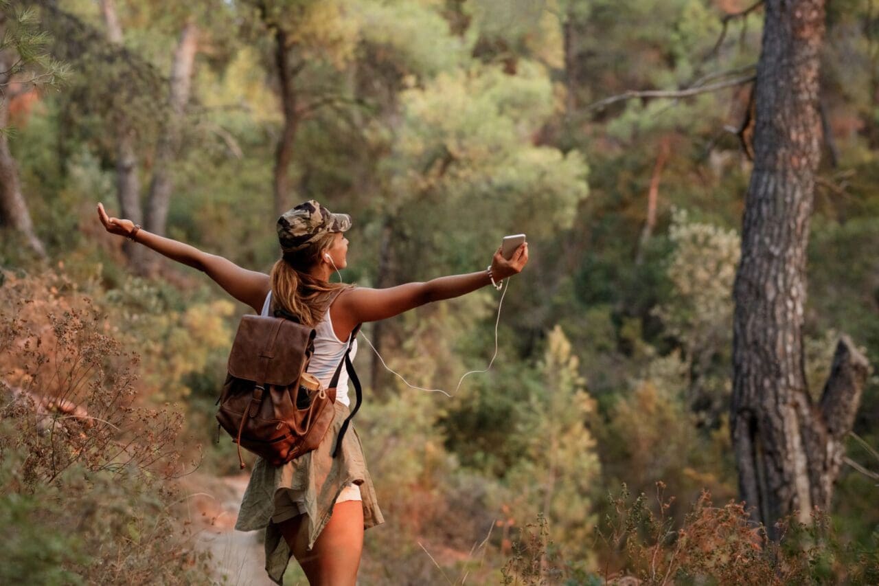 Back view of woman having fun while walking through forest with arms outstretched