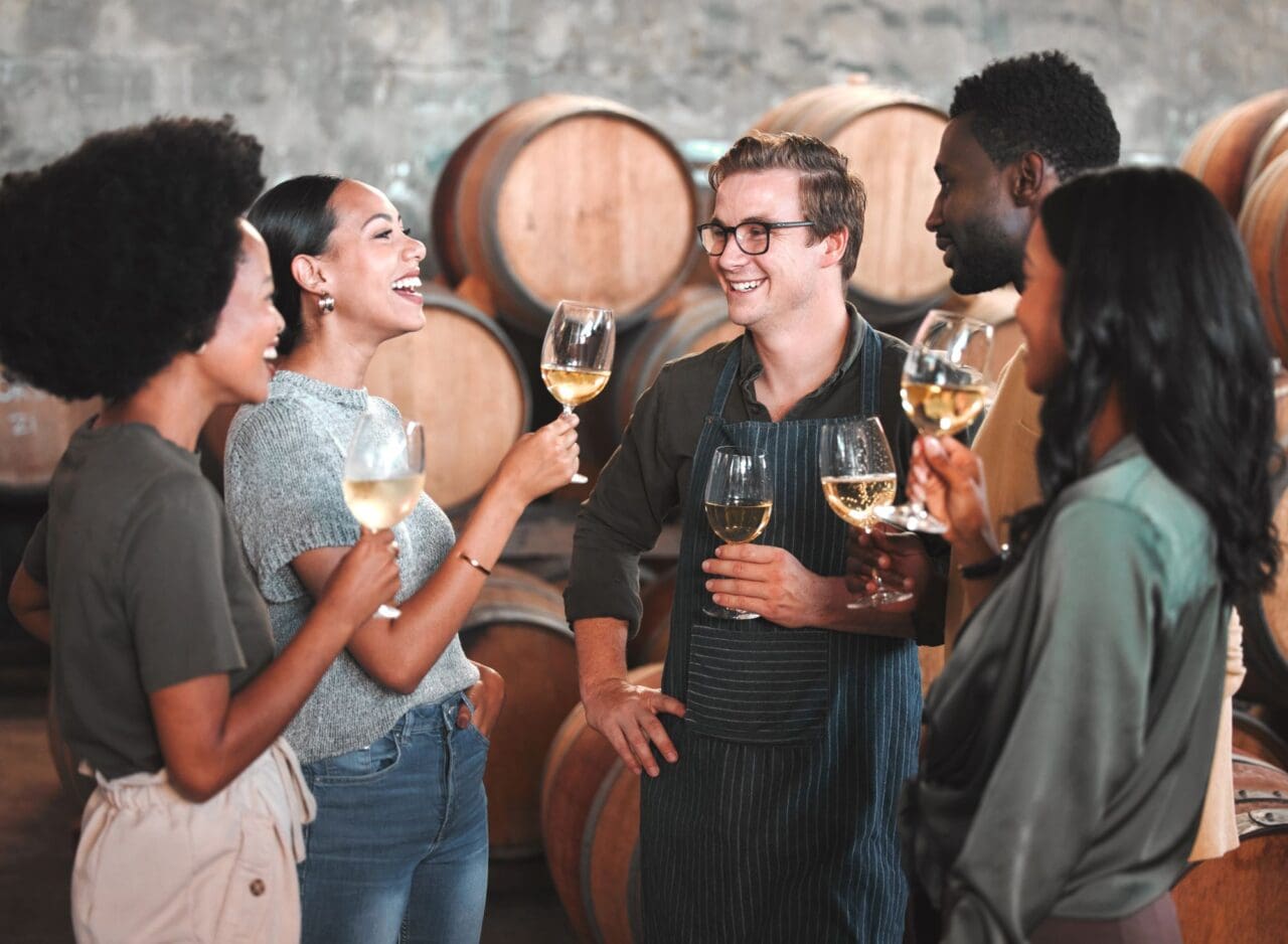 Group of friends wine tasting at a distillery or cellar drinking glasses and enjoying the tour together