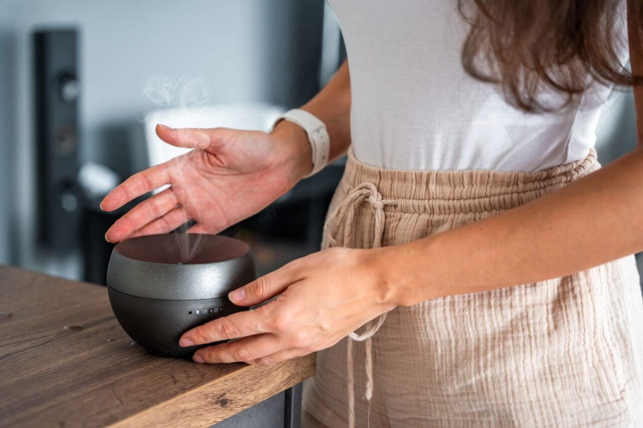 Woman turned on the grey aroma oil diffuser on light table at home, air freshener-essential oils